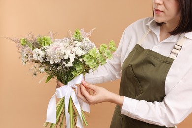 Photo of Florist with beautiful bouquet of flowers on beige background, closeup