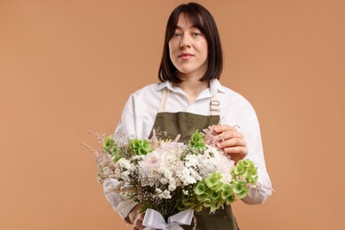 Photo of Florist with beautiful bouquet of flowers on beige background