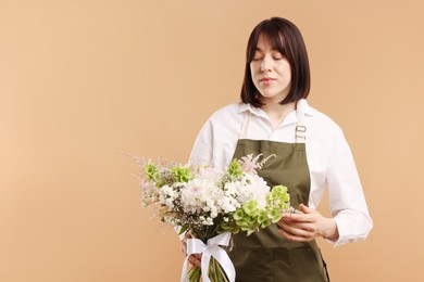 Photo of Florist with beautiful bouquet of flowers on beige background, space for text
