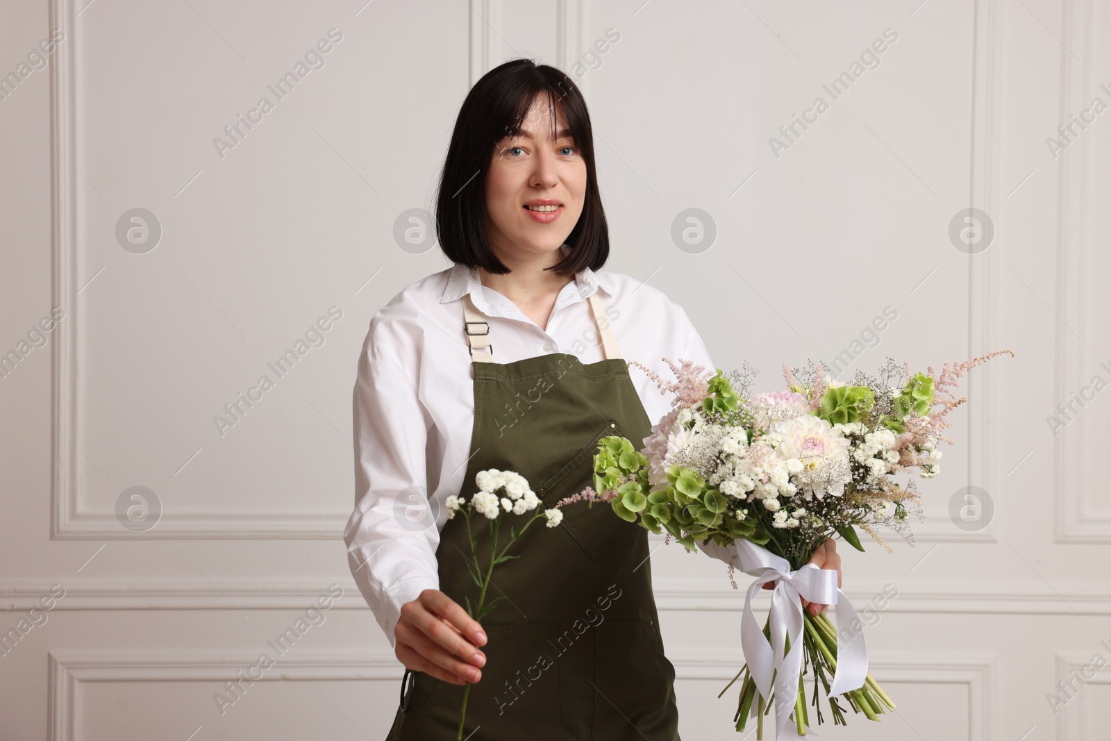 Photo of Florist with beautiful bouquet of flowers near white wall indoors