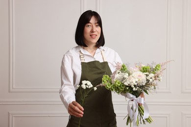 Photo of Florist with beautiful bouquet of flowers near white wall indoors
