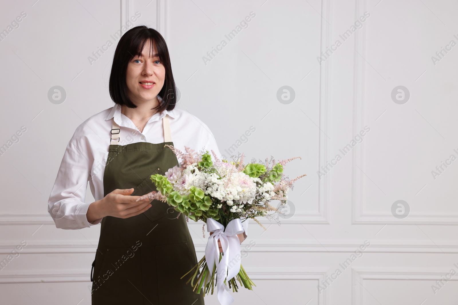 Florist with beautiful bouquet of flowers near white wall indoors, space for text Photo of Florist with beautiful bouquet of flowers near white wall indoors, space for text