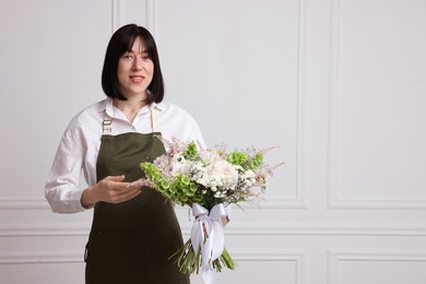 Photo of Florist with beautiful bouquet of flowers near white wall indoors, space for text