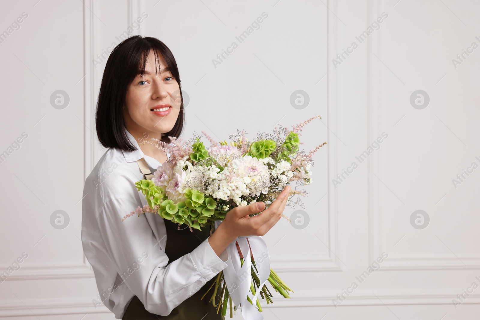 Florist with beautiful bouquet of flowers near white wall indoors, space for text Photo of Florist with beautiful bouquet of flowers near white wall indoors, space for text