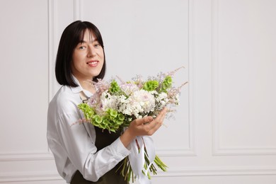 Photo of Florist with beautiful bouquet of flowers near white wall indoors, space for text