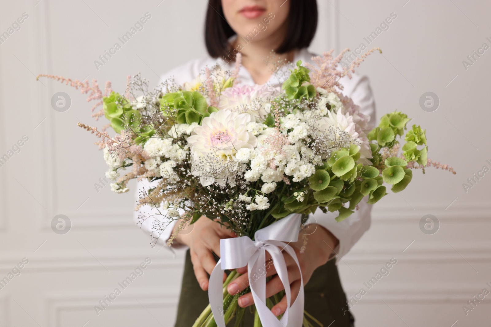 Florist with beautiful bouquet of flowers near white wall indoors, closeup Photo of Florist with beautiful bouquet of flowers near white wall indoors, closeup
