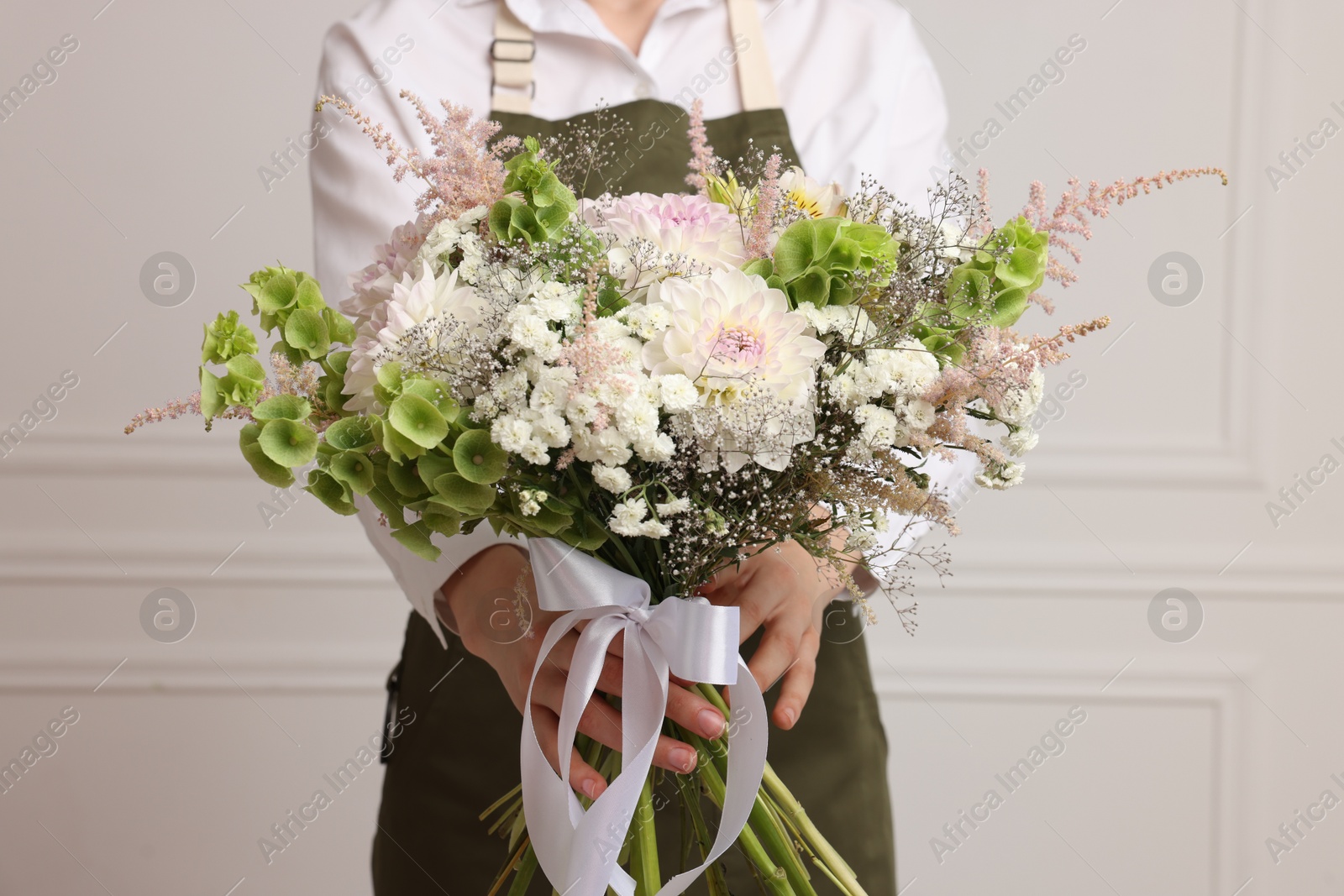 Photo of Florist with beautiful bouquet of flowers near white wall indoors, closeup