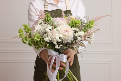 Photo of Florist with beautiful bouquet of flowers near white wall indoors, closeup