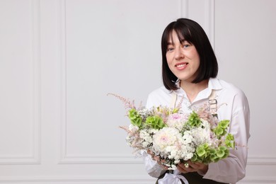 Photo of Florist with beautiful bouquet of flowers near white wall indoors, space for text