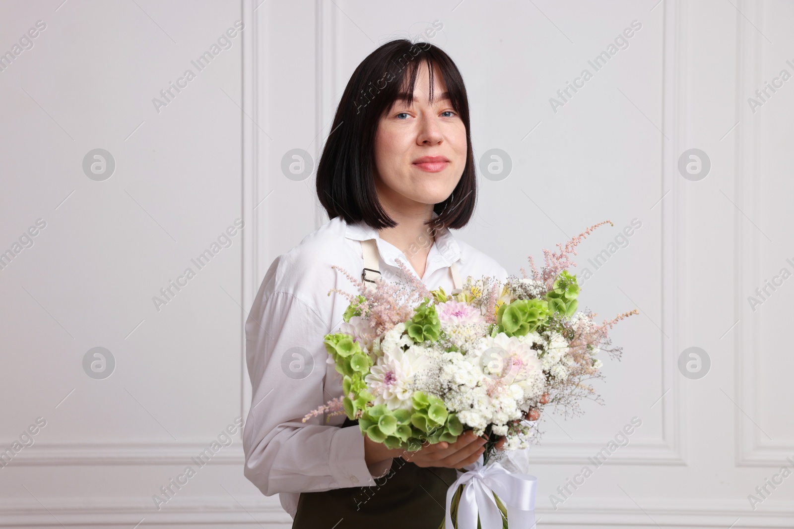 Photo of Florist with beautiful bouquet of flowers near white wall indoors