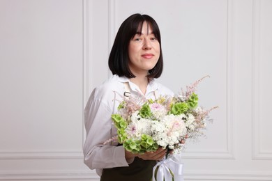 Photo of Florist with beautiful bouquet of flowers near white wall indoors