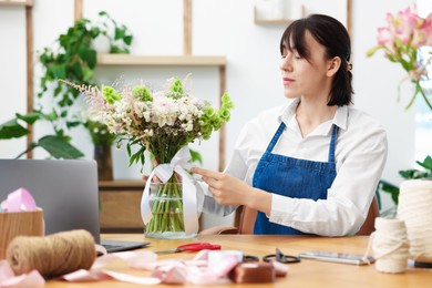 Photo of Florist making bouquet of flowers at wooden table indoors