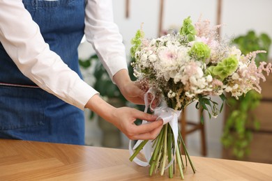 Photo of Florist making bouquet of flowers at wooden table indoors, closeup