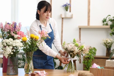 Photo of Florist making bouquet of flowers at wooden table indoors