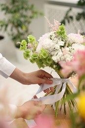 Photo of Florist making bouquet of flowers at table indoors, closeup