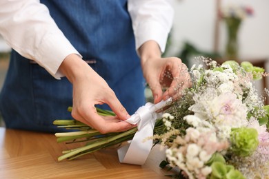 Photo of Florist making bouquet of flowers at wooden table indoors, closeup