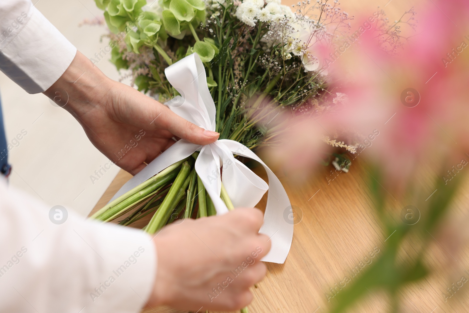 Florist making bouquet of flowers at wooden table indoors, closeup Photo of Florist making bouquet of flowers at wooden table indoors, closeup