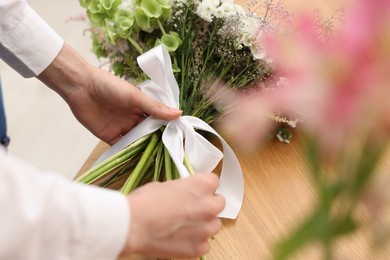 Photo of Florist making bouquet of flowers at wooden table indoors, closeup
