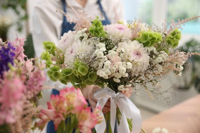 Photo of Florist with beautiful bouquet of flowers indoors, selective focus