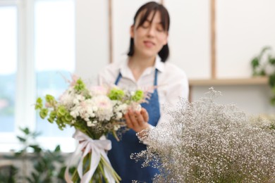 Photo of Florist with beautiful bouquet of flowers indoors, selective focus