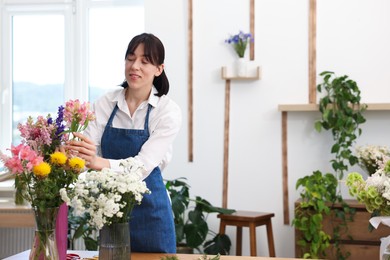 Photo of Florist making bouquet of flowers in shop, space for text