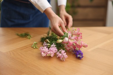 Photo of Florist making bouquet of flowers at wooden table indoors, closeup