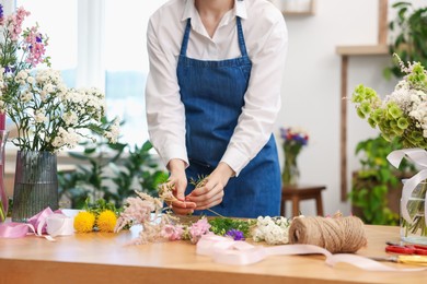 Photo of Florist making bouquet of flowers at table indoors, closeup