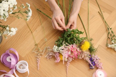 Photo of Florist making bouquet of flowers at wooden table, top view