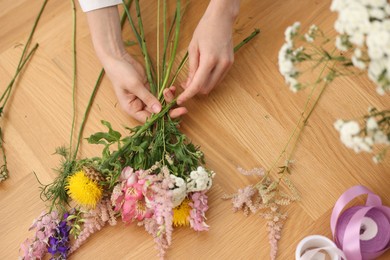 Photo of Florist making bouquet of flowers at wooden table, top view