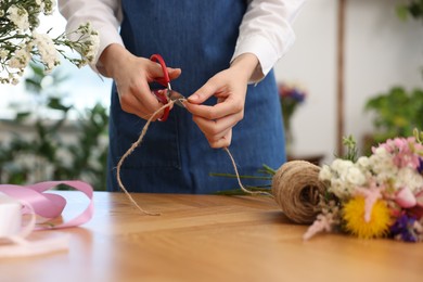 Photo of Florist making bouquet of flowers at wooden table indoors, closeup