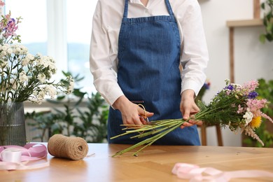 Photo of Florist making bouquet of flowers at wooden table indoors, closeup