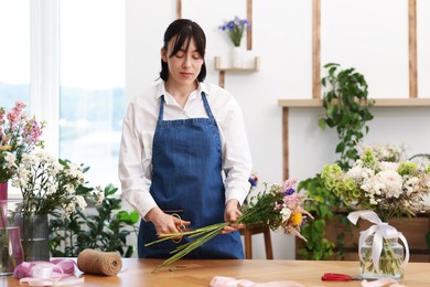 Photo of Florist making bouquet of flowers at wooden table indoors
