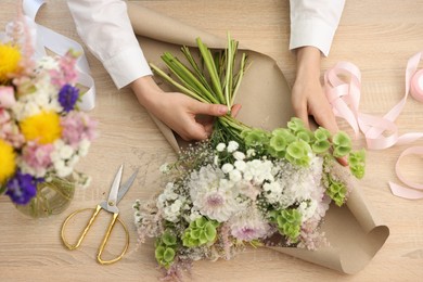 Photo of Florist making bouquet of flowers at wooden table, top view