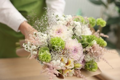Photo of Florist making bouquet of flowers at table indoors, closeup