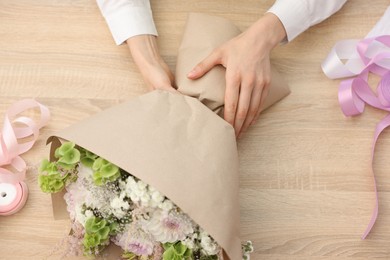 Photo of Florist making bouquet of flowers at wooden table, top view
