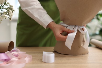 Photo of Florist making bouquet of flowers at wooden table indoors, closeup