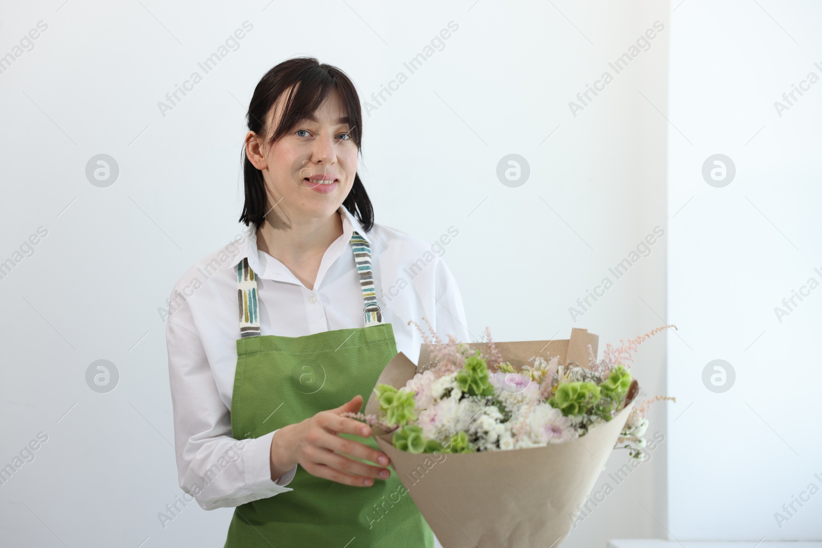 Photo of Florist with beautiful bouquet of flowers near white wall indoors