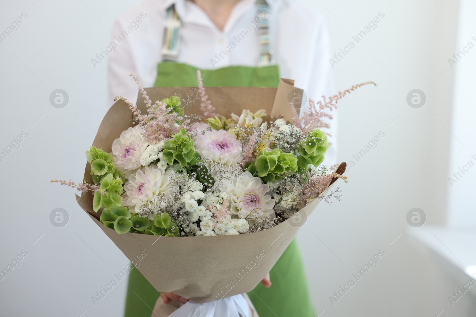 Florist with beautiful bouquet of flowers near white wall indoors, closeup Photo of Florist with beautiful bouquet of flowers near white wall indoors, closeup