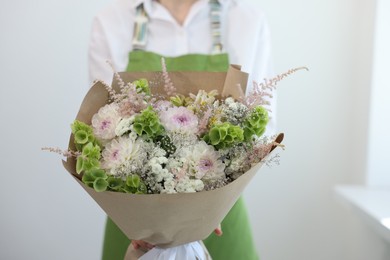 Photo of Florist with beautiful bouquet of flowers near white wall indoors, closeup