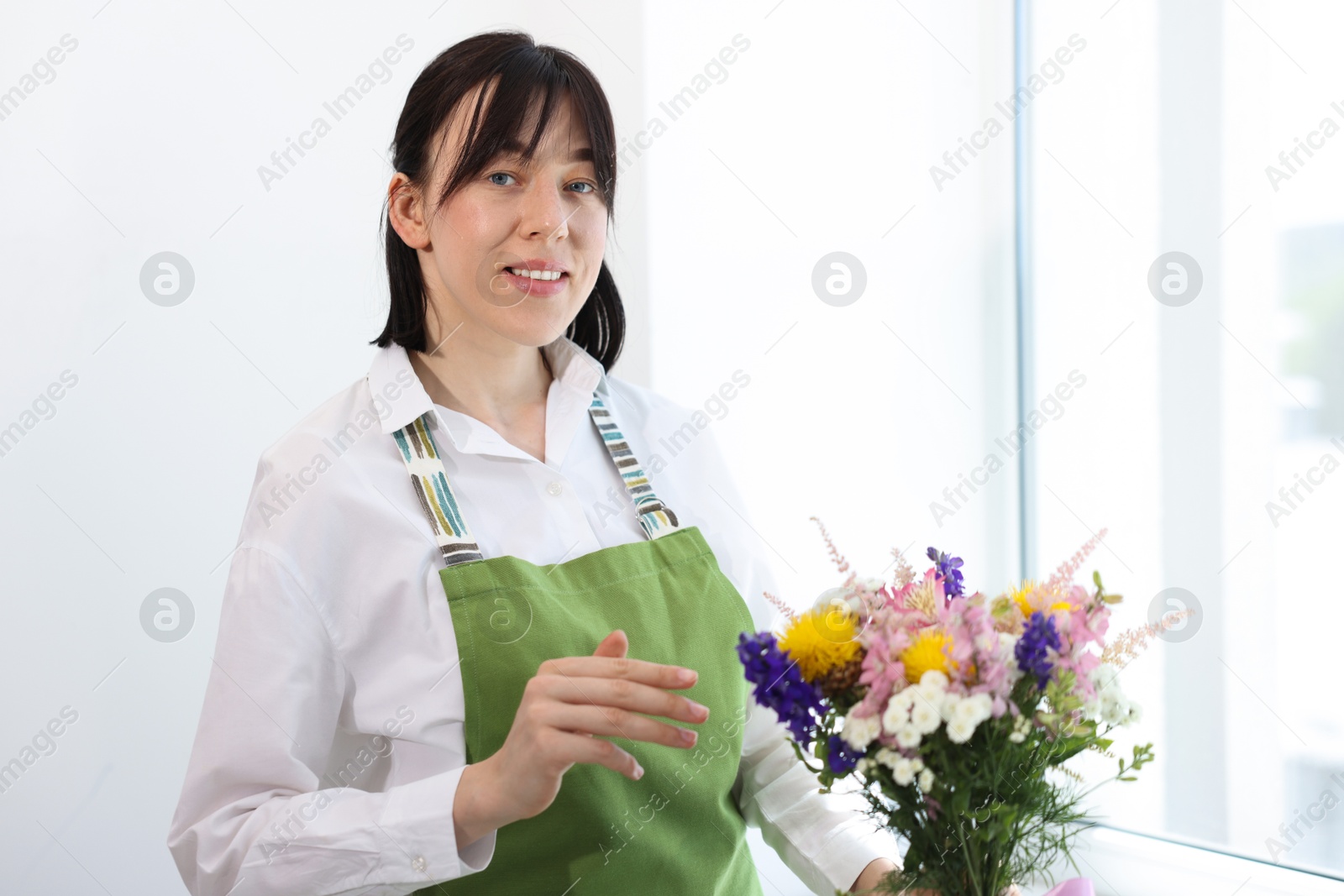 Florist with beautiful bouquet of flowers near window indoors Photo of Florist with beautiful bouquet of flowers near window indoors