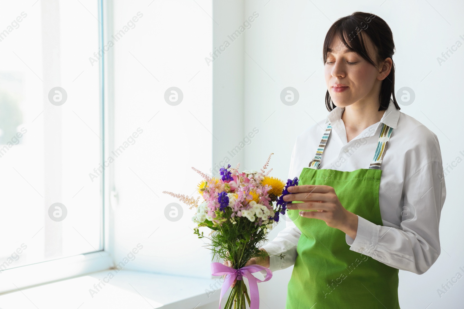 Florist with beautiful bouquet of flowers near window indoors Photo of Florist with beautiful bouquet of flowers near window indoors