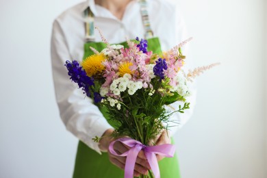 Photo of Florist with beautiful bouquet of flowers near white wall indoors, closeup