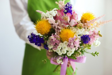 Photo of Florist with beautiful bouquet of flowers near white wall indoors, closeup