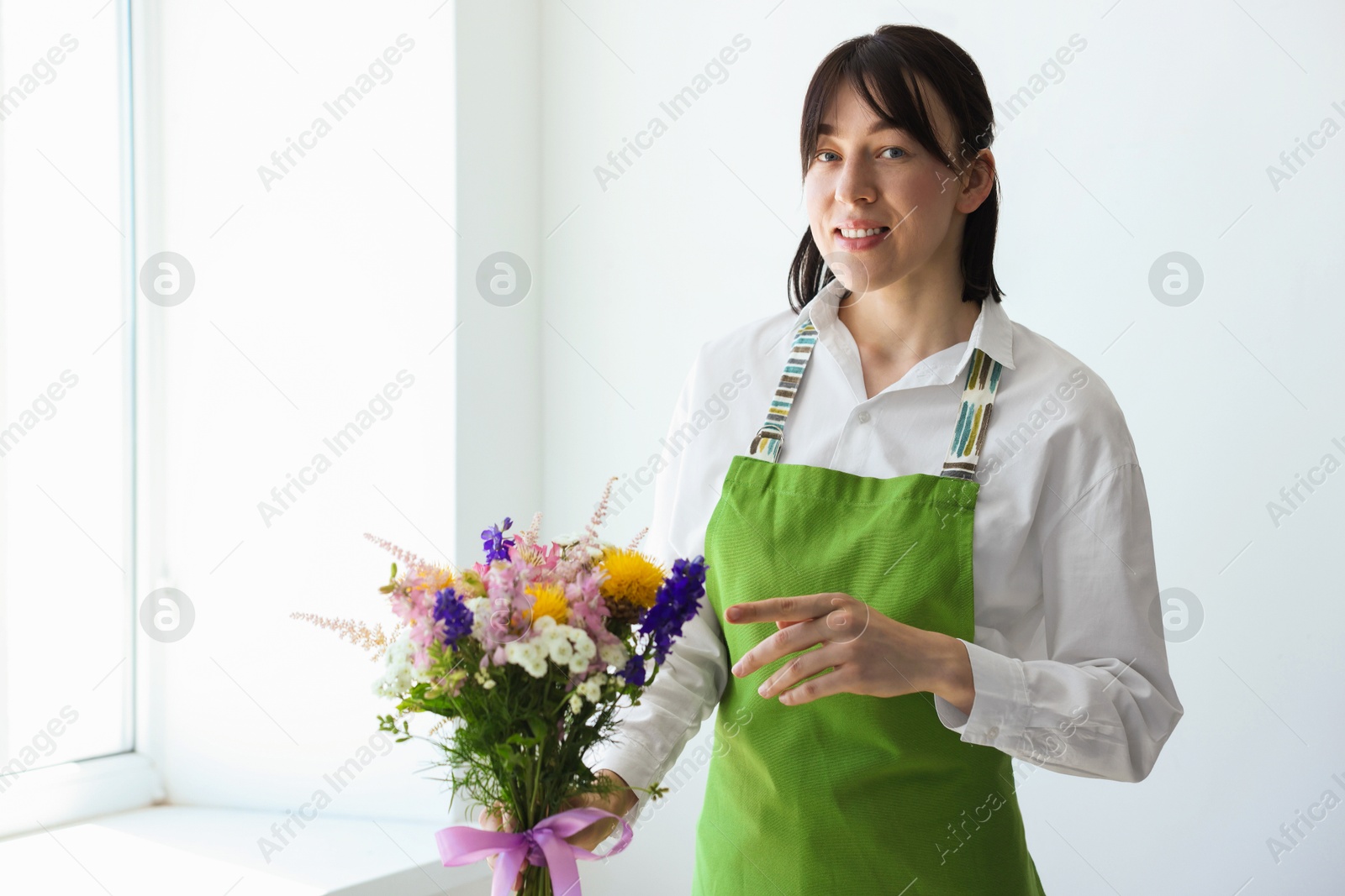 Florist with beautiful bouquet of flowers near window indoors Photo of Florist with beautiful bouquet of flowers near window indoors