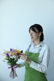 Photo of Florist with beautiful bouquet of flowers near white wall indoors