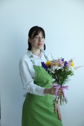 Photo of Florist with beautiful bouquet of flowers near white wall indoors