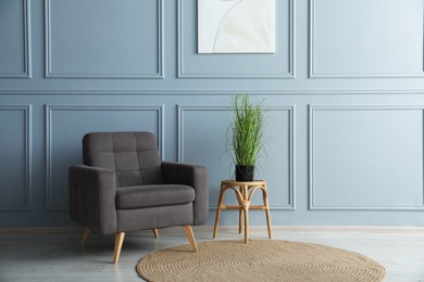 Photo of Comfortable armchair and houseplant near light blue wall indoors