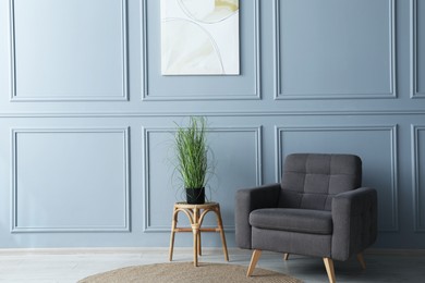 Photo of Comfortable armchair and houseplant near light blue wall indoors. Space for text