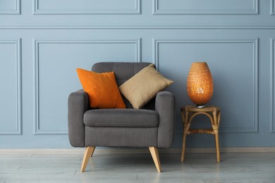 Photo of Comfortable armchair and lamp near light blue wall indoors