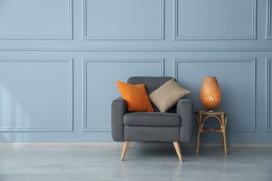 Photo of Comfortable armchair and lamp near light blue wall indoors. Space for text